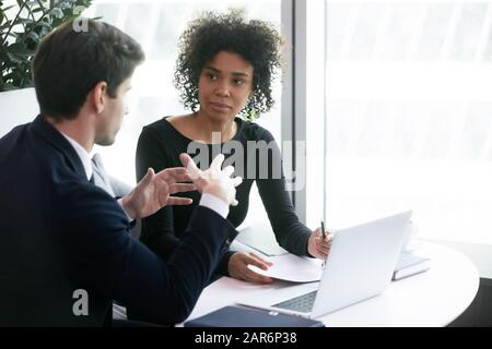 Junge afroamerikanische Managerin, die auf eine selbstbewusste männliche Führungskraft hört. Stockfoto