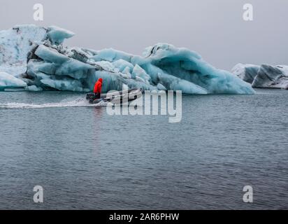 Mann mit roter Jacke auf einem motorisierten Zodiac Tour Boot, Ponton, Floß, Island, Europa Jokulsarlon Glacier Lagoon, Ostisländischer Eisdiamantstrand Stockfoto