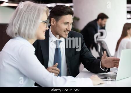 Lächelnder Geschäftsmann, der Projektpräsentation für einen reifen Kunden vorzeigt. Stockfoto