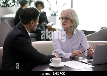 Fokussierte Unternehmer führen Geschäftsverhandlungen mit älteren Partnerinnen. Stockfoto