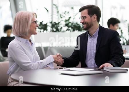 Angenehme Geschäftsfrau mittleren Alters schüttelt mit lächelnden jungen Geschäftsleuten die Hände. Stockfoto