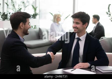 Lächelnde Geschäftsleute in Anzügen schütteln nach Unterzeichnung der Vereinbarung die Hände. Stockfoto