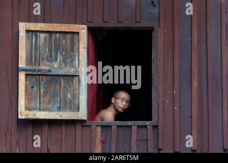 Nyaungshwe, Myanmar - 26. Dezember 2019: Ein junger Mönch, der im Kloster Shwe Yanp Yay aus dem Fenster schaut. Dieses Kloster besteht ganz aus Teak Stockfoto