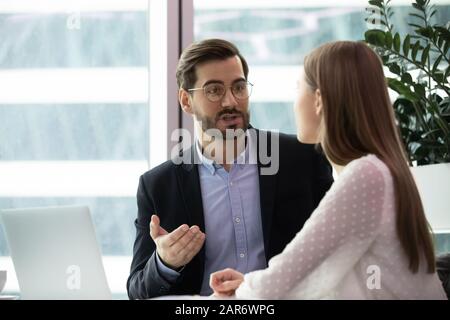 Konzentrierter männlicher Teamleiter, der junge Praktikantin im Büro betreut. Stockfoto