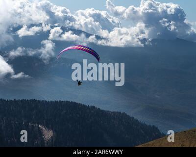 Ein Mann auf Gleitschirm fliegt durch die Wolken über Wald und Gebirge. Stockfoto