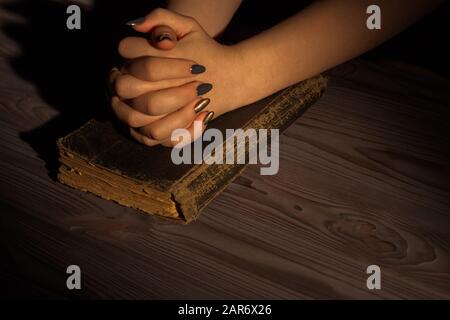 Frau betet mit gefalteten Händen auf einer alten heiligen bibel. Stockfoto