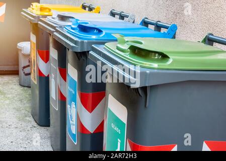 Reihe von Recyclingbehältern mit bunten Deckeln entlang der äußeren Rückwand eines Hauses Stockfoto