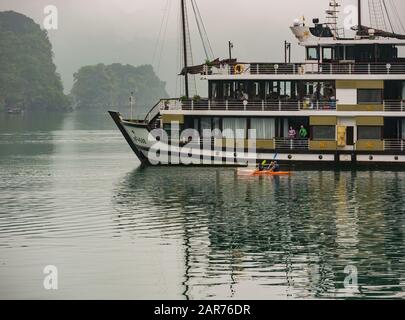 Kreuzfahrtschiff Azalea bei nebeligem Wetter mit Touristen in Kajak- und Kalksteinfelsen, Halong Bay, Vietnam, Asien Stockfoto