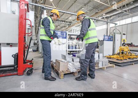 Zwei Arbeiter tragen in der CNC-Maschinenhalle Aluminium-Billet Stockfoto