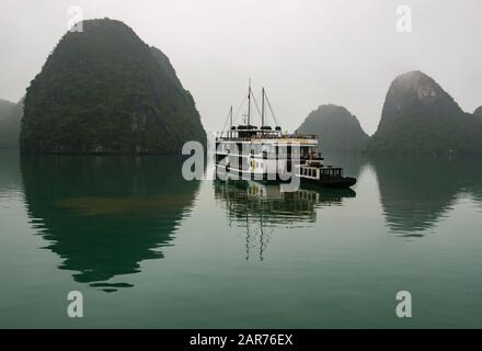 Das Kreuzfahrtschiff von Tourist Azalea ankerte bei nebeligem Wetter mit Kalksteinkarstfelsen, die sich im Meer, der Halong Bay, Vietnam, Asien widerspiegeln Stockfoto