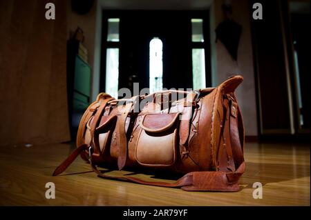 In der Nähe der Haustür eines Privathauses steht eine Ledertasche mit Sachen. Hinter der Tasche sieht man die Haustür und dahinter das Sonnenlicht Stockfoto