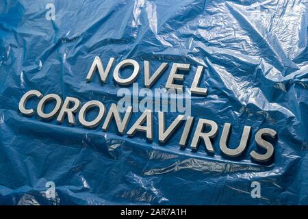 Die Worte Novel Coronavirus mit silbernen Metallbuchstaben auf gelegt Zerknitterte blaue Plastikfolie - diagonale Zusammensetzung Stockfoto