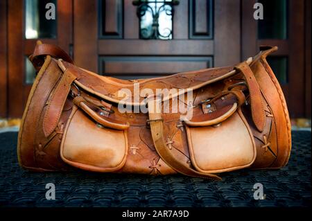 Eine orangefarbene, stilvolle Reisetasche aus Leder steht auf einer Gummimatte am Eingang zu einem Privathaus. Nahaufnahme Stockfoto