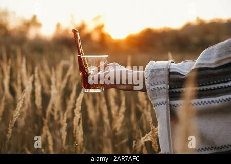 Handspritzen von heißem Kaffee aus der Glasbecher in sonnigem warmen Licht auf dem Hintergrund ländlicher Kräuter. Alternative Kaffeezubereitung auf Reisen. Atmospheri Stockfoto