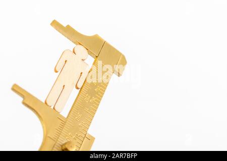 Makro kleine lasergeschnittene Holzfigur und Messing-Zirkel gegen den weißlichen BG. Messung von persönlichen Leistungsindikatoren, demografischen Daten, Produktivität, Stockfoto