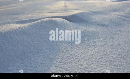 Abstrakter Winterhintergrund - Textur der reinen Schneeoberfläche mit Schneeverwehungen im Sonnenlicht. Licht und Schatten auf weißer, schneebedeckter Kulisse bei sonnigem Wetter Stockfoto