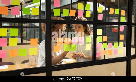 Konzentrierte multiethnische Frauen arbeiten an Projekten auf bunten Aufklebern Stockfoto