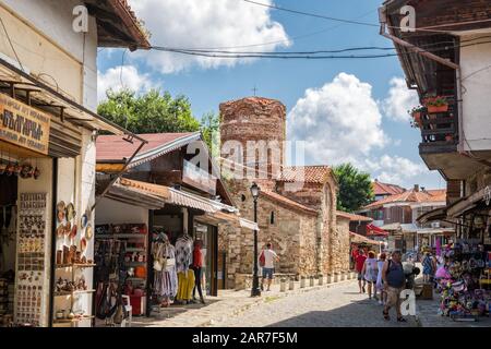 Nessebar, BULGARIEN - 26. JUNI 2019: Alte Johannes-der-Täufer-Kirche (11. Jahrhundert) und Souvenirläden in Der Altstadt von Nessebar. Die Leute gehen entlang von na Stockfoto