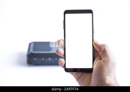 Mann Hand hält leeres Bildschirm-Smartphone und verbindet sich über das Heimmodem im Internet. WiFi-Verbindungskonzept. Stockfoto