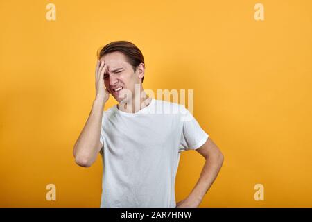 Der junge Mann in weißem T-Shirt hat gesundheitliche Probleme. Kopfschmerzen legen Hand in Kopf Stockfoto