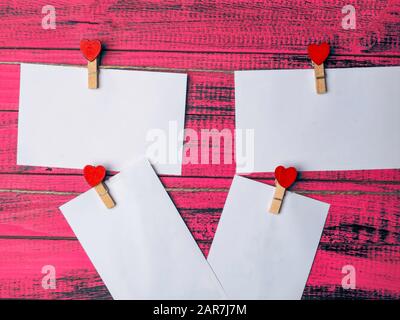 Leere Aufkleber und rotes Herz aus Holz auf Stoffstiften, die an einem Seil an einer alten, rauen Holzwand hängen Stockfoto