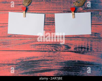 Leere Aufkleber und rotes Herz aus Holz auf Stoffstiften, die an einem Seil an einer alten, rauen Holzwand hängen Stockfoto
