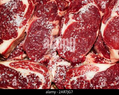 Frisches rohes Rindersteak mit Salz auf Holzschneidebrett, Draufsicht Stockfoto