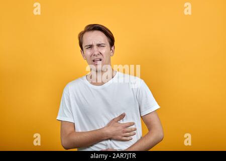 Magenschmerzen Magenprobleme weißes T-Shirt junger Mann auf gelbem Hintergrund. Stockfoto