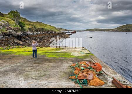 Ein weiblicher Tourist, der Fotos auf einem Handy im Fischerdorf Little Killary nahe der Einmündung von Killary Harbour, Connemara, County Galway, machte Stockfoto