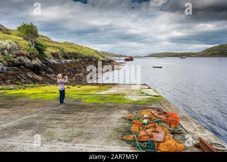 Ein weiblicher Tourist, der Fotos auf einem Handy im Fischerdorf Little Killary nahe der Einmündung von Killary Harbour, Connemara, County Galway, machte Stockfoto