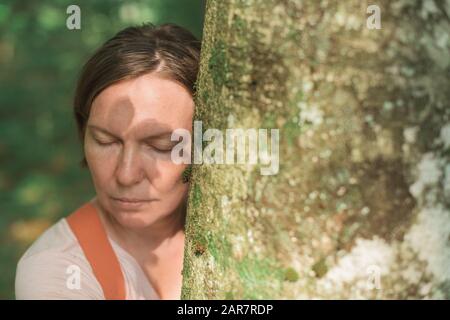 Frau umarmt Baumstamm im Wald, weibliche Umweltschützerin mit ihren Armen um den Baum, selektiver Fokus Stockfoto