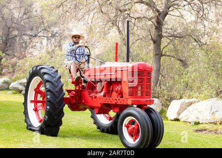 Gutaussehender Mann mit Sonnenbrille, der den Traktor fährt, um auf dem Bauernhof zu arbeiten Stockfoto