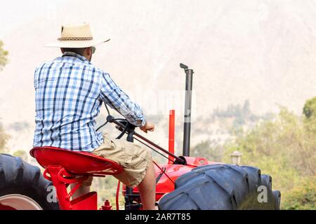 Gutaussehender Mann mit Sonnenbrille, der den Traktor fährt, um auf dem Bauernhof zu arbeiten Stockfoto