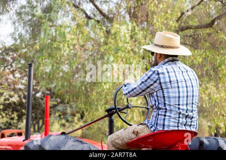 Gutaussehender Mann mit Sonnenbrille, der den Traktor fährt, um auf dem Bauernhof zu arbeiten Stockfoto