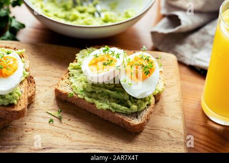 Toast mit Avocado und gekochtem Ei, garniert mit Mikrogrüns auf einem Holztisch. Gesundes Frühstück Stockfoto