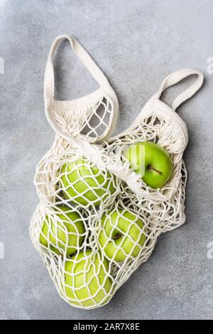 Mesh-Einkaufstasche mit grünen Äpfeln auf grauem Betongrund. Draufsicht. Null-Abfall-Konzept, gesundes, umweltfreundliches Lifestyle-Konzept Stockfoto