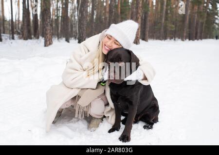 Junge liebevoll lächelnde Frau, die schwarze Vergeltung umarmte, die auf Schnee sitzt Stockfoto