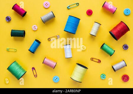Flaches Lay mit Spulen aus farbigem Gewinde, Knöpfen und Sicherheitsstiften auf gelbem Hintergrund Stockfoto
