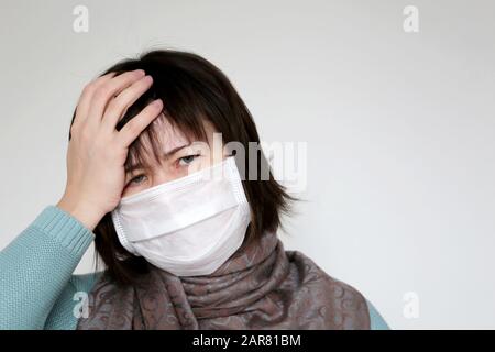 Unglückliche Frau in medizinischer Maske hält die Hand an der Stirn. Konzept von Krankheit, Fieber, Kälte und Grippe, Kopfschmerzen, Coronavirus-Symptome Stockfoto