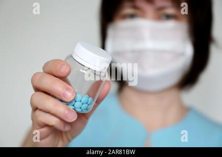 Arzt mit Pillen, Frau in medizinischer Maske mit einer Flasche blauer Tabletten. Konzept der Dosis von Medikamenten, Vitaminen, medizinischen Untersuchungen, Coronavirus, Grippe-Behandlung Stockfoto