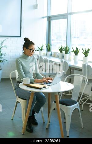 Junge, ernsthafte weibliche Freiberuflerin oder Studentin, die vor dem Laptop tippt Stockfoto