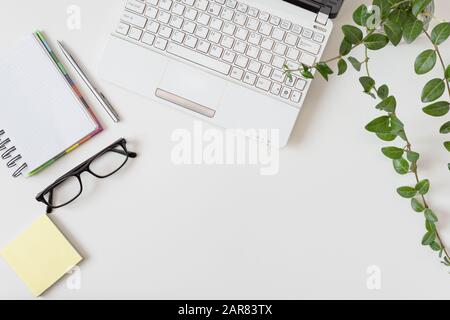 Arbeitsbereich mit Laptop, Tagebuch und anderen Objekten auf weißem Hintergrund. Eleganter Schreibtisch in weißer Farbe mit Blumentopf. Kopierbereich. Flaches Lay. Stockfoto