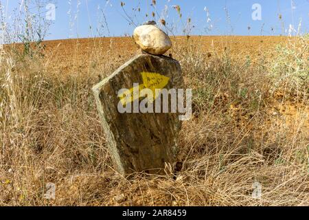 Gelber Pfeil auf einem Stein, der den Weg entlang der Route des Camino di Santiago di Compostela in Spanien markiert Stockfoto