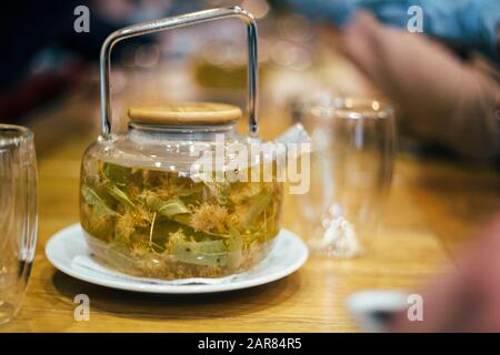 Teekanne Linden-Tee und Blumen auf Holztisch im Café. Kräutertee Stockfoto