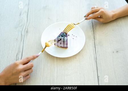 Hände von zwei jungen Weibchen mit Gabeln, die ein Stück köstlichem Dessert einnehmen Stockfoto