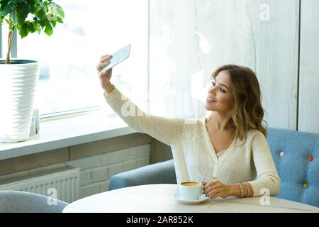 Ziemlich junge lächelnde Frau mit Smartphone macht selfie, während sie im Café ruht Stockfoto