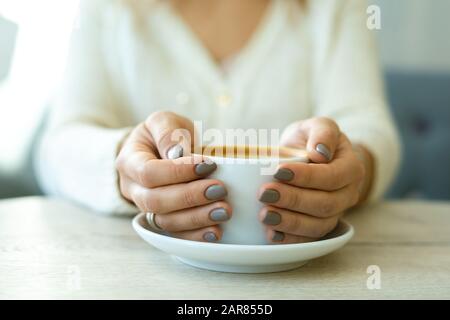 Hände junger, erholsamer Frauen, die Porzellanbecher mit frischem heißem Cappuccino halten Stockfoto