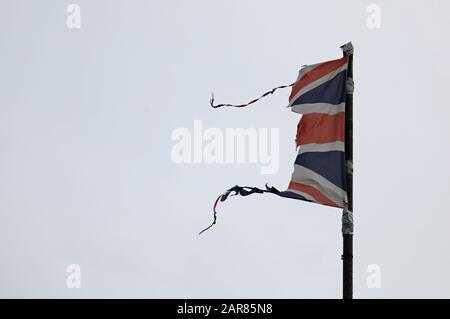 Union Jack, britische Flagge, zerfetzelt, gerissen, fliegen und flattern auf einem grauen Pfosten mit grauem Himmel könnte eine Katastrophe wie Krieg, Sturm oder Brexit illustrieren. Stockfoto