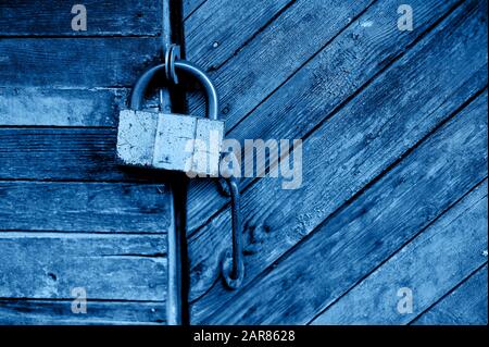 Alte grüne Tür oder Wand eines Holzhauses im rustikalen Stil, mit abblätternder Farbe.an der Tür hängt ein altes Metallschloss, Classic blau. Der Trend 2020. Stockfoto