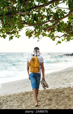 Guy Tourist mit gelbem Rucksack geht am Strand entlang am Meer. Stockfoto